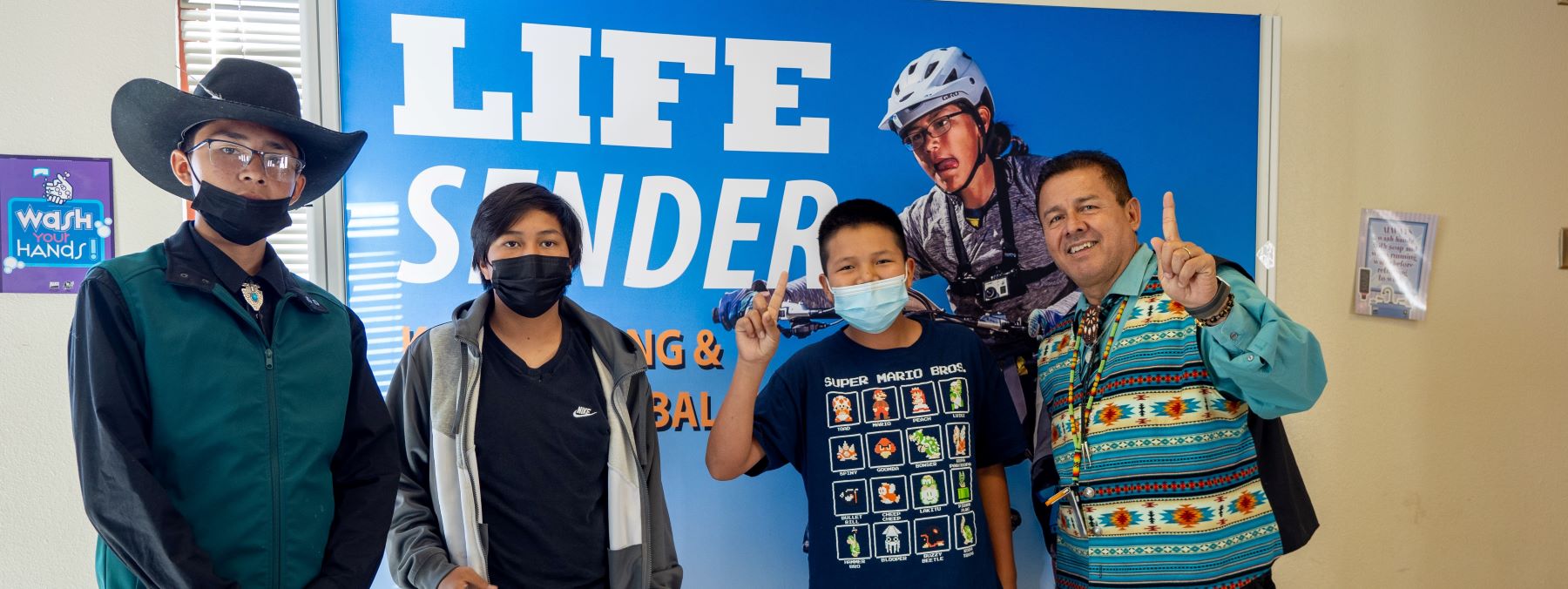 Prinicipal and three students posing in front of sign.