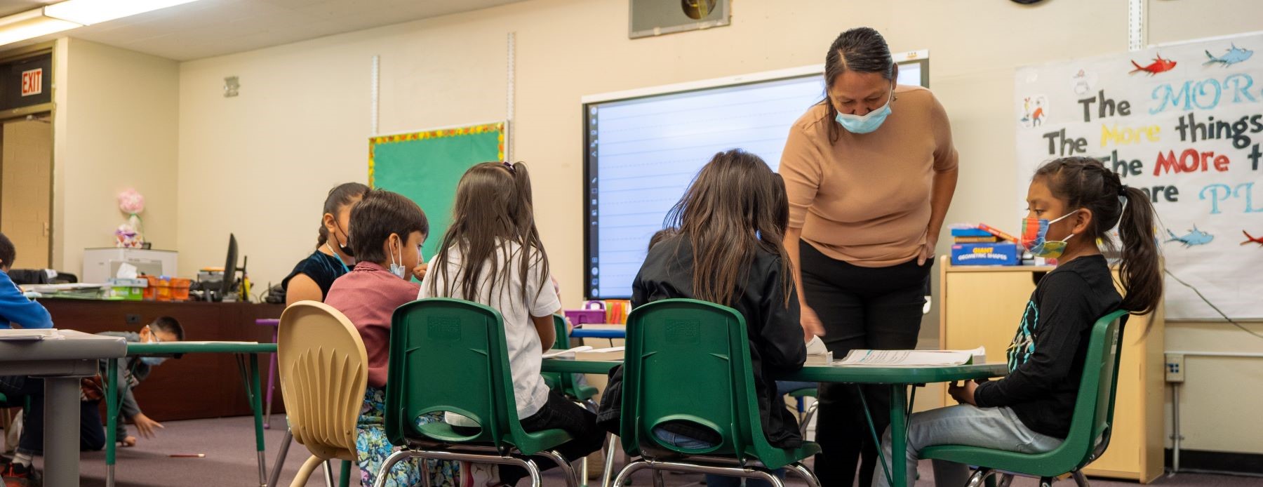 teacher instructing students sitting together at a table in classroom