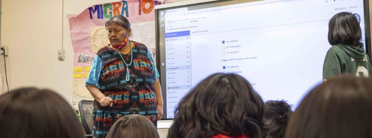 Female staff teaching in the front of the classroom by a digital screen