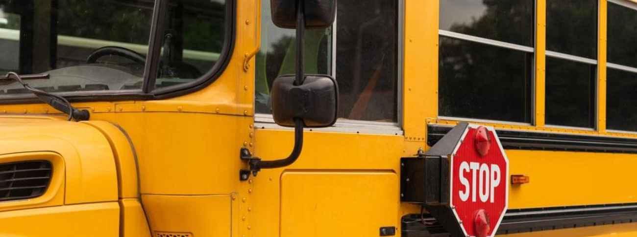 Close-up of a yellow school bus showing the driver's side, windows, side mirrors, and an extended red stop sign.